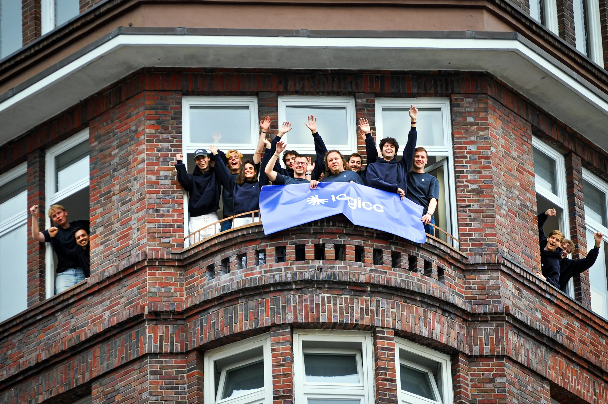 Das Logicc-Team winkt mit dem Logicc-Banner aus den Fenstern des Büros in Hamburg